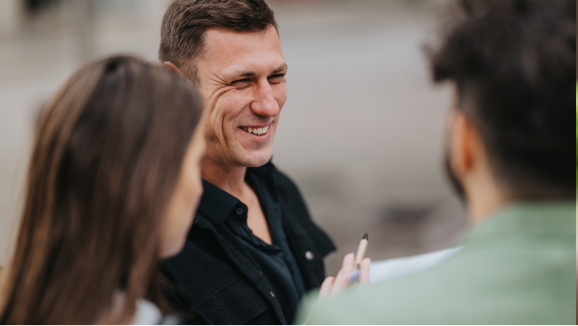 A man smiles at two coworkers during a meeting.