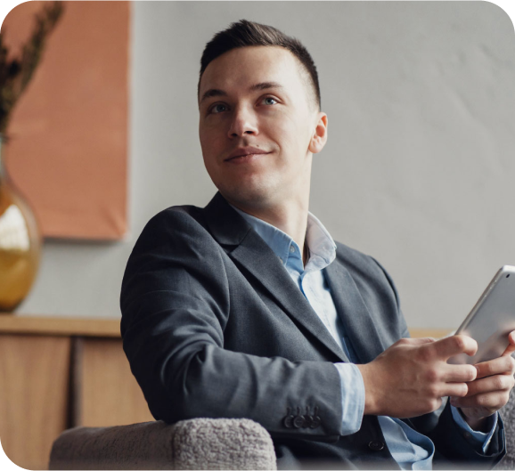 A young man in a blue suite holding a tablet and a smile on his face