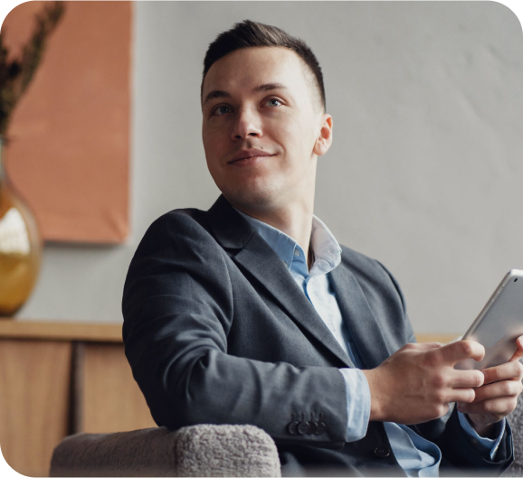 A young man in a blue suite holding a tablet and a smile on his face