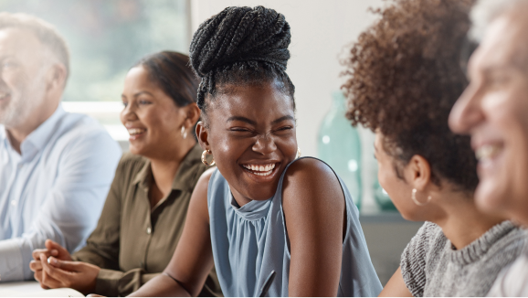 A woman smiles at her coworker seated next to her at a group meeting.