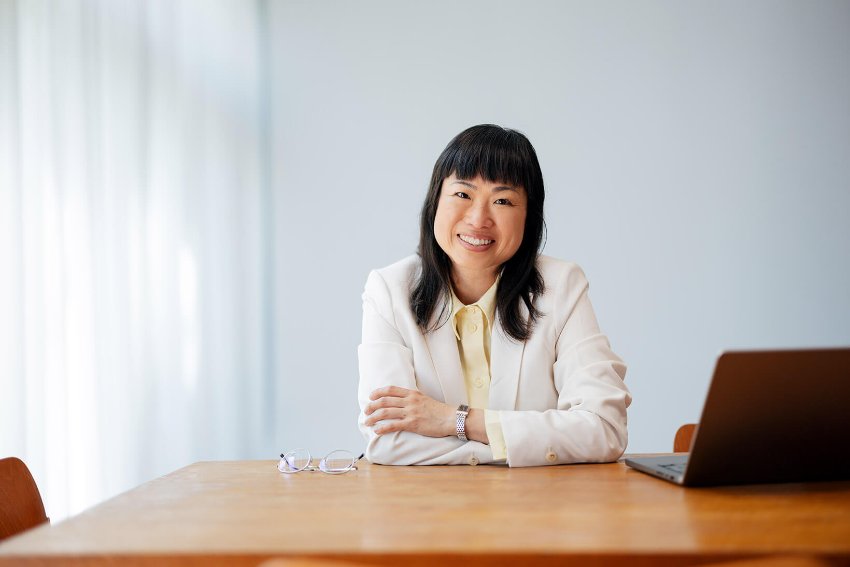 A well-dressed, suited woman sitting at a desk and working on her laptop