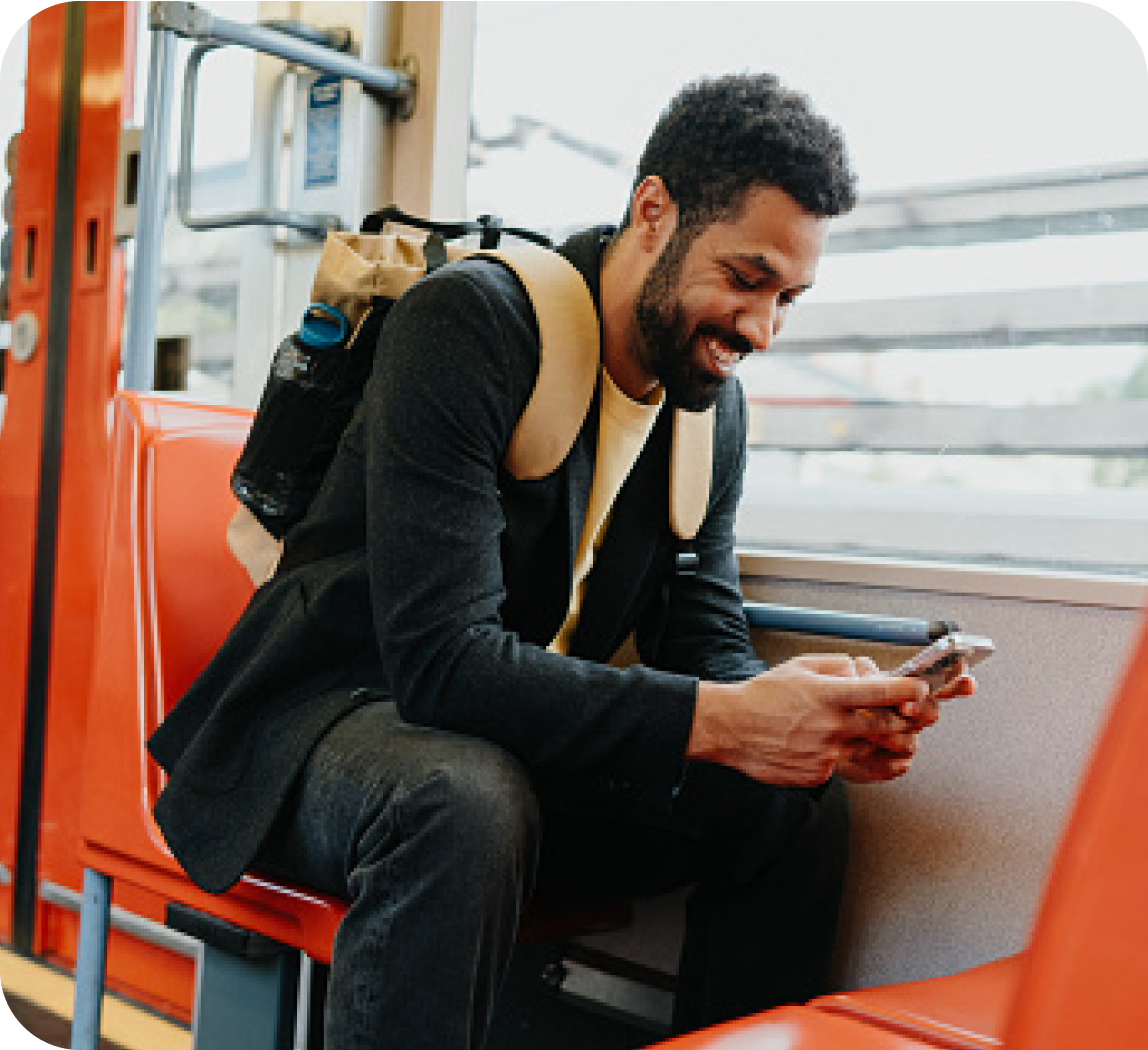 A young man with a backpack travelling in a public transport and checking his phone with a smile on his face