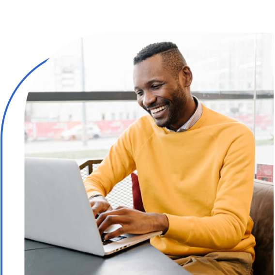 A man in a yellow t-shirt working on a laptop with a smile on his face