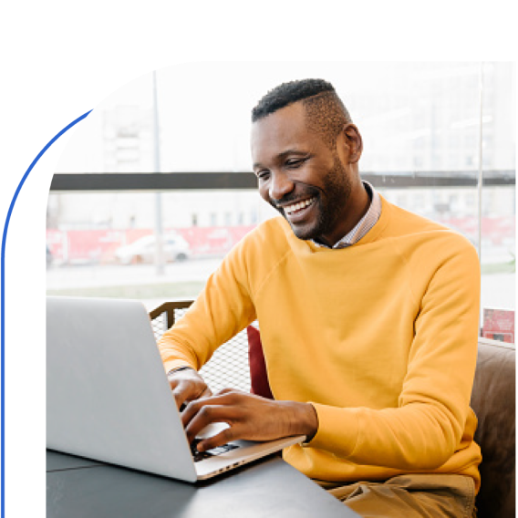 A man in a yellow t-shirt working on a laptop with a smile on his face