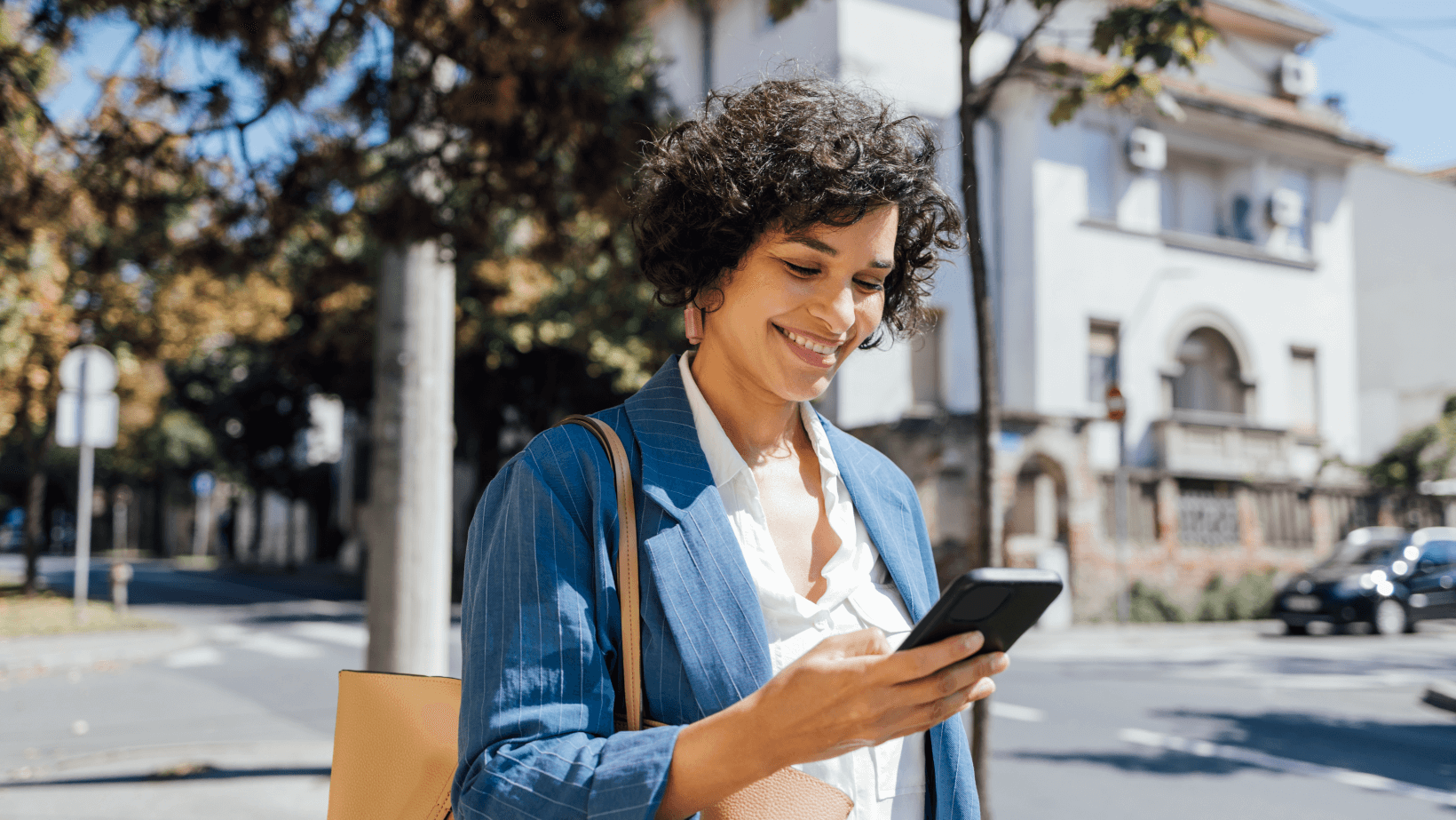 A smiling woman in a blue blazer checking her phone