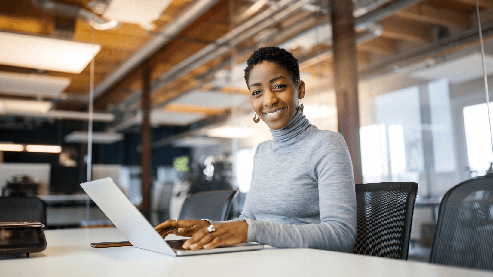 A young woman with a smile working on a laptop sitting at office desk