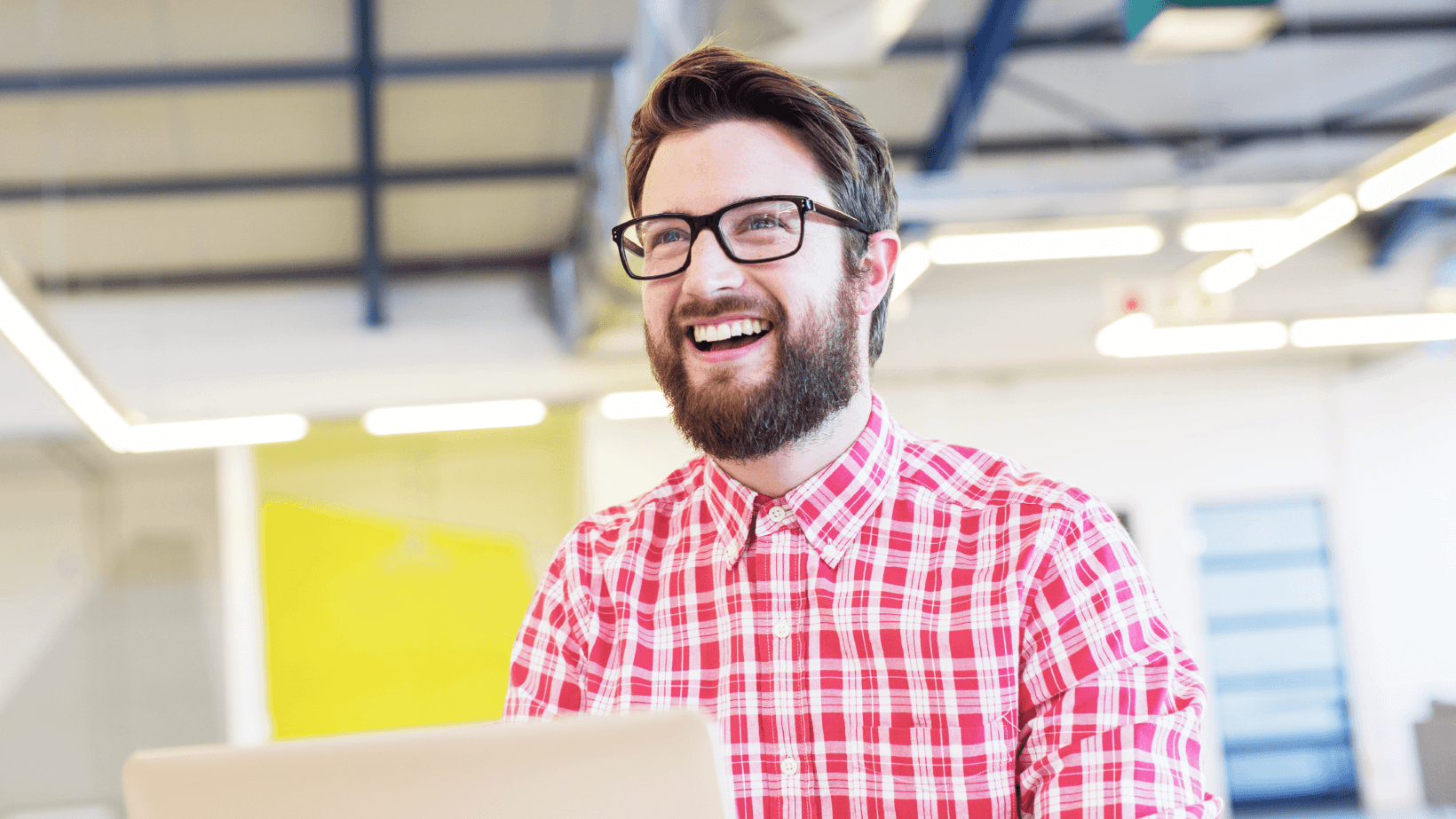 A young man working on a laptop with a smile at workplace