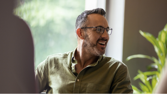 A man wearing glasses smiles while looking to the side.
